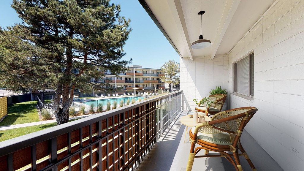 A balcony with a chair and a table is overlooking a pool.