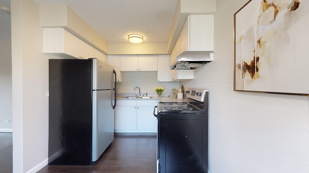 A black refrigerator stands in a kitchen with white cabinets and a black dishwasher.