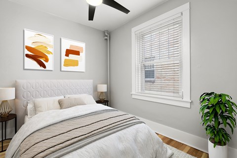 A bedroom with a bed, two lamps, a plant, and two paintings on the wall.