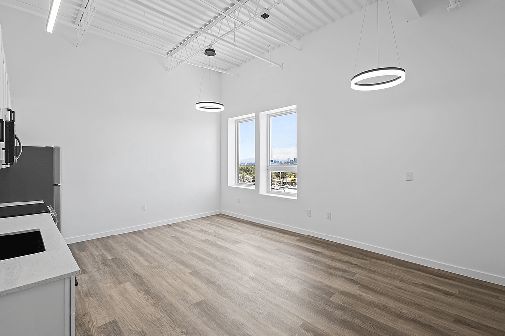 A spacious room with a kitchen area on the left and a window with a view of trees outside.
