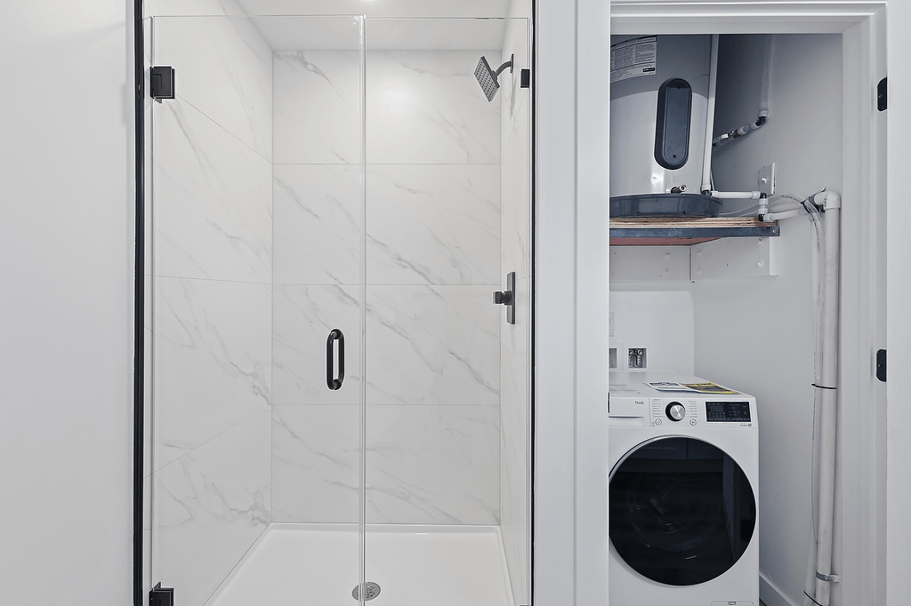 A white bathroom with a marble wall and a washing machine in the doorway.