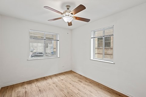 A room with a ceiling fan and two windows.