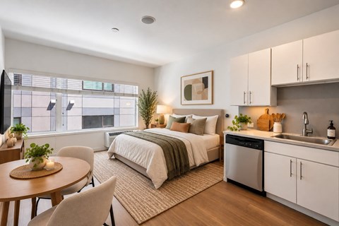 A modern bedroom with a large bed, a kitchenette, and a dining area.