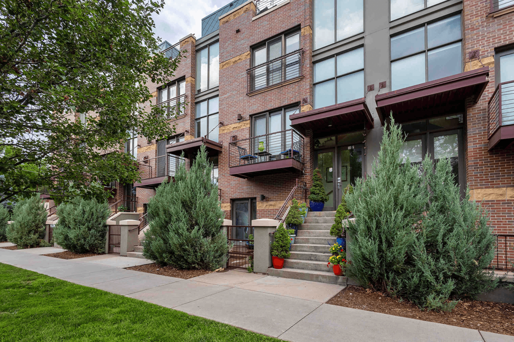 the front of a brick apartment building with stairs and trees in front