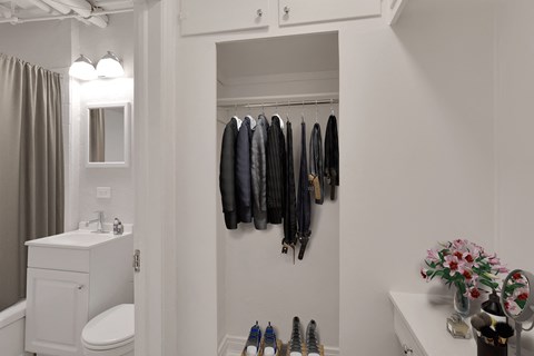 A white bathroom with a toilet, sink, and a coat rack with several coats hanging on it.