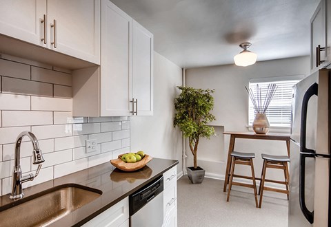 A kitchen with a black fridge, white cabinets, and a black dishwasher.