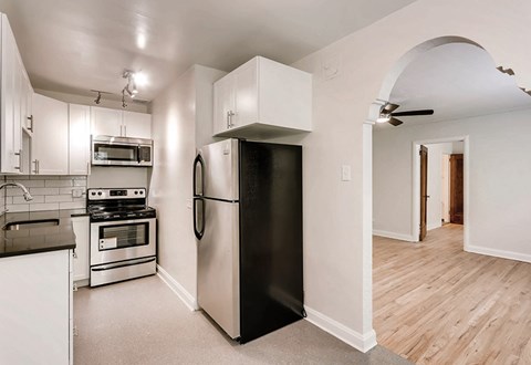 A black refrigerator is in a white kitchen with wood floors.