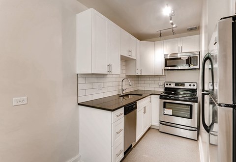 A kitchen with white cabinets and black countertops.