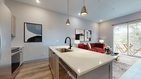 A modern kitchen with a large island and a red couch in the background.