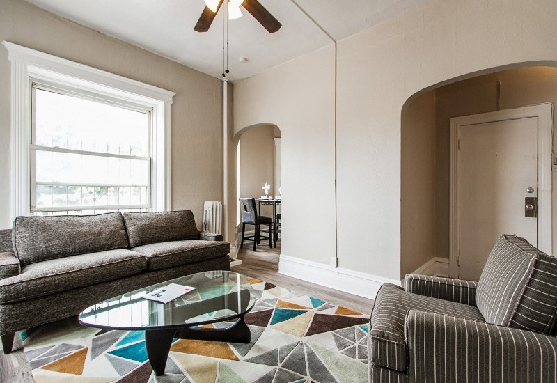 A living room with a grey couch, a glass coffee table, and a ceiling fan.
