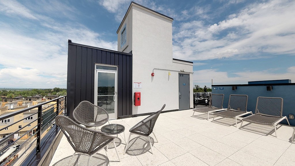 A patio with chairs and a table is in front of a white building.