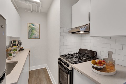 A kitchen with a stove, a bowl of fruit, and a painting on the wall.