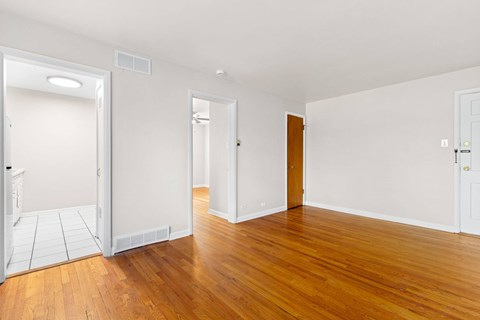 A room with wooden floors and white walls with a door on the left and a window on the right.