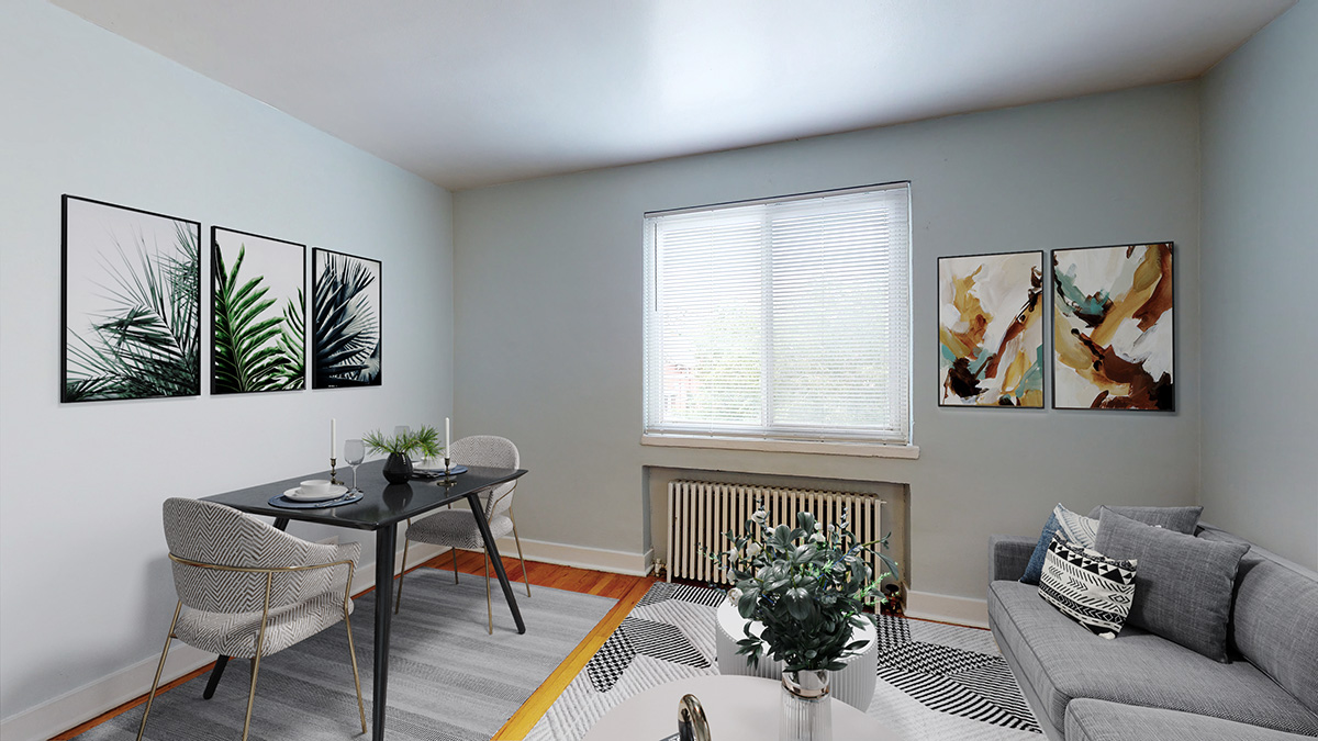 A living room with a grey couch, a dining table with chairs, and three framed pictures on the wall.