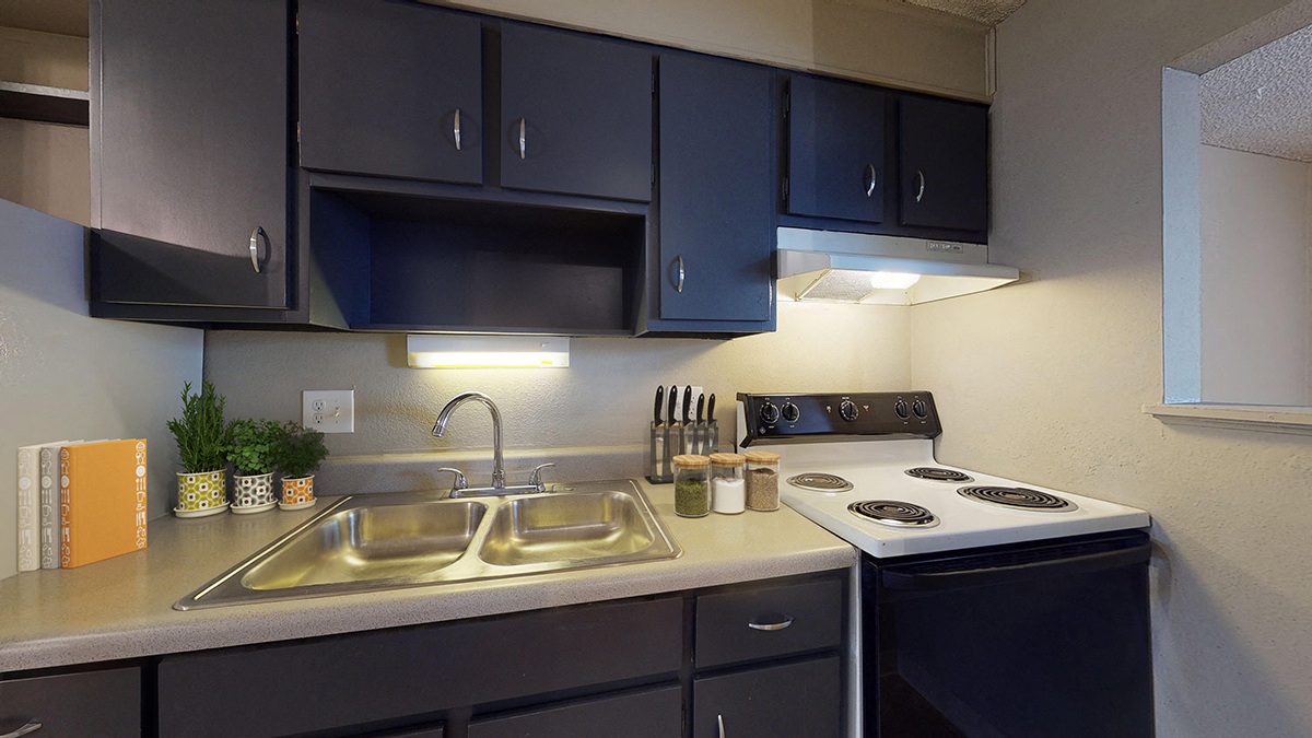 A kitchen with a stove, sink, and cabinets.
