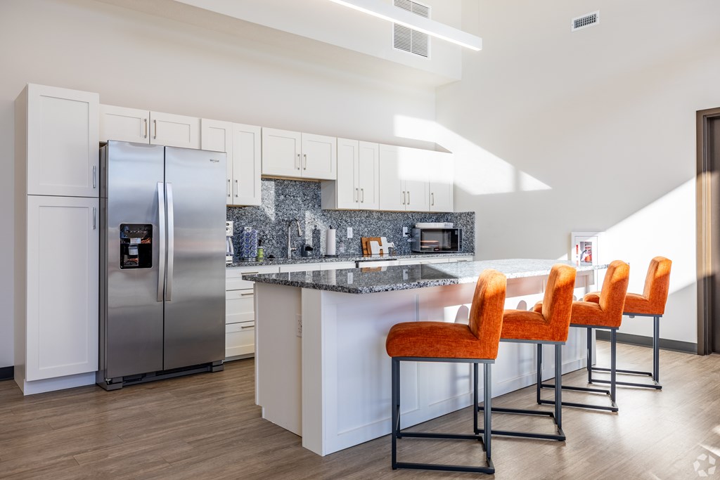 A kitchen with a refrigerator, bar stools, and a marble countertop.