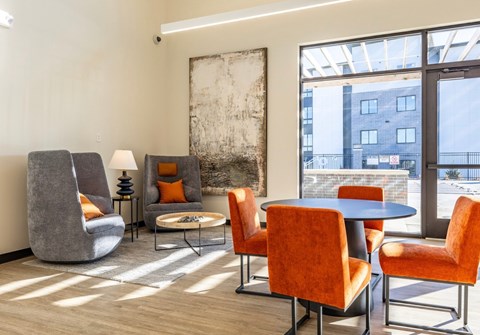 A modern living room with a grey chair, orange chairs, and a large abstract painting on the wall.