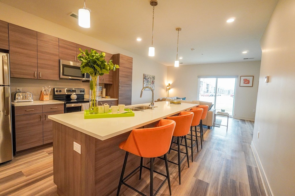 a kitchen with a long island with orange chairs
