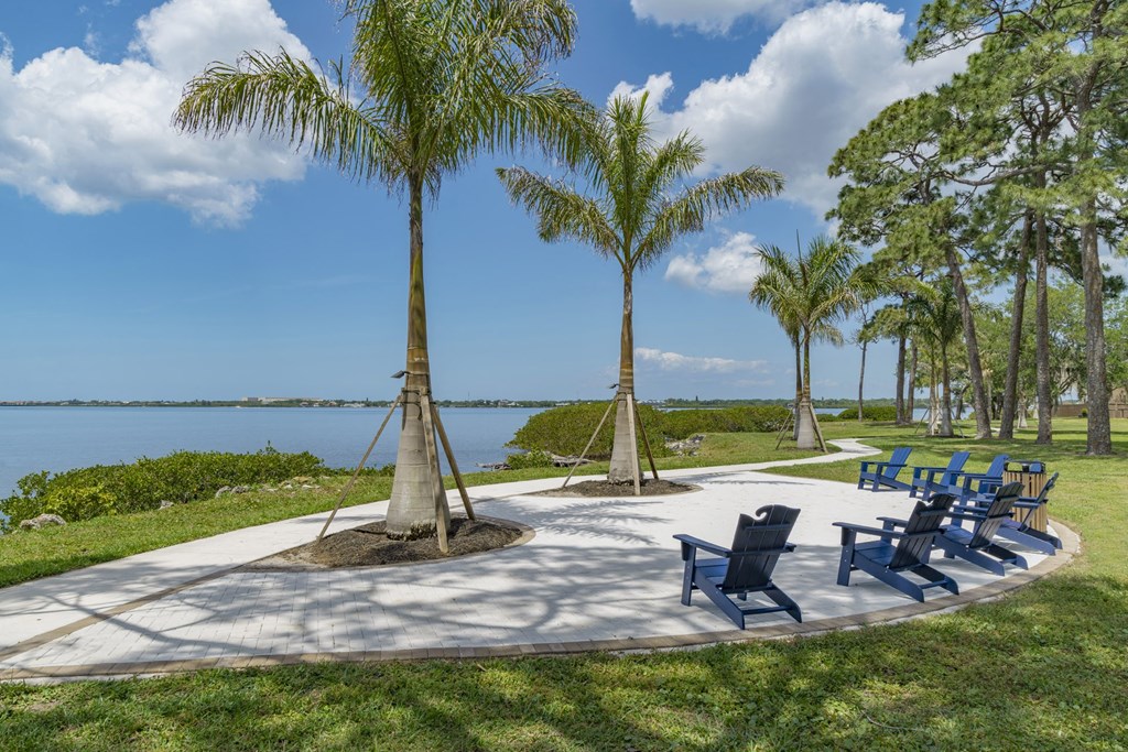 a patio with chairs and palm trees near the water