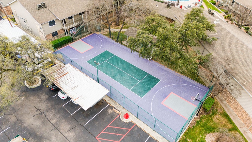 an aerial view of a tennis court and a basketball court with trees and a house