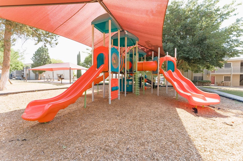 a playground with two slides and a swing set  at Cantera Apartments, El Paso TX 79935
