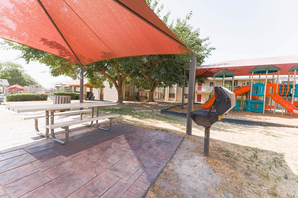 a picnic table with an umbrella in front of a playground  at Cantera Apartments, El Paso TX 79935