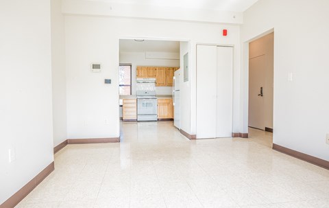 an empty living room with a kitchen in the background