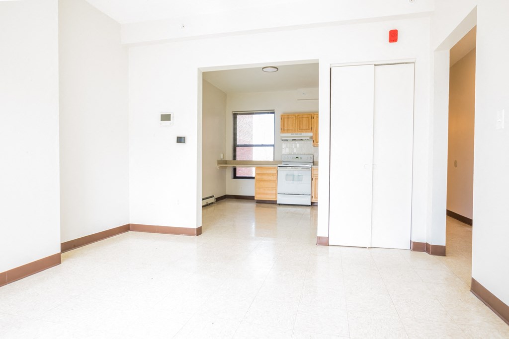 an empty living room with a kitchen in the background