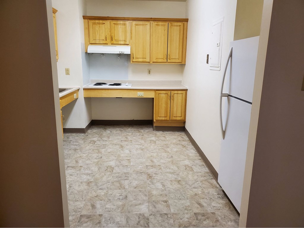 an empty kitchen with wooden cabinets and a white refrigerator