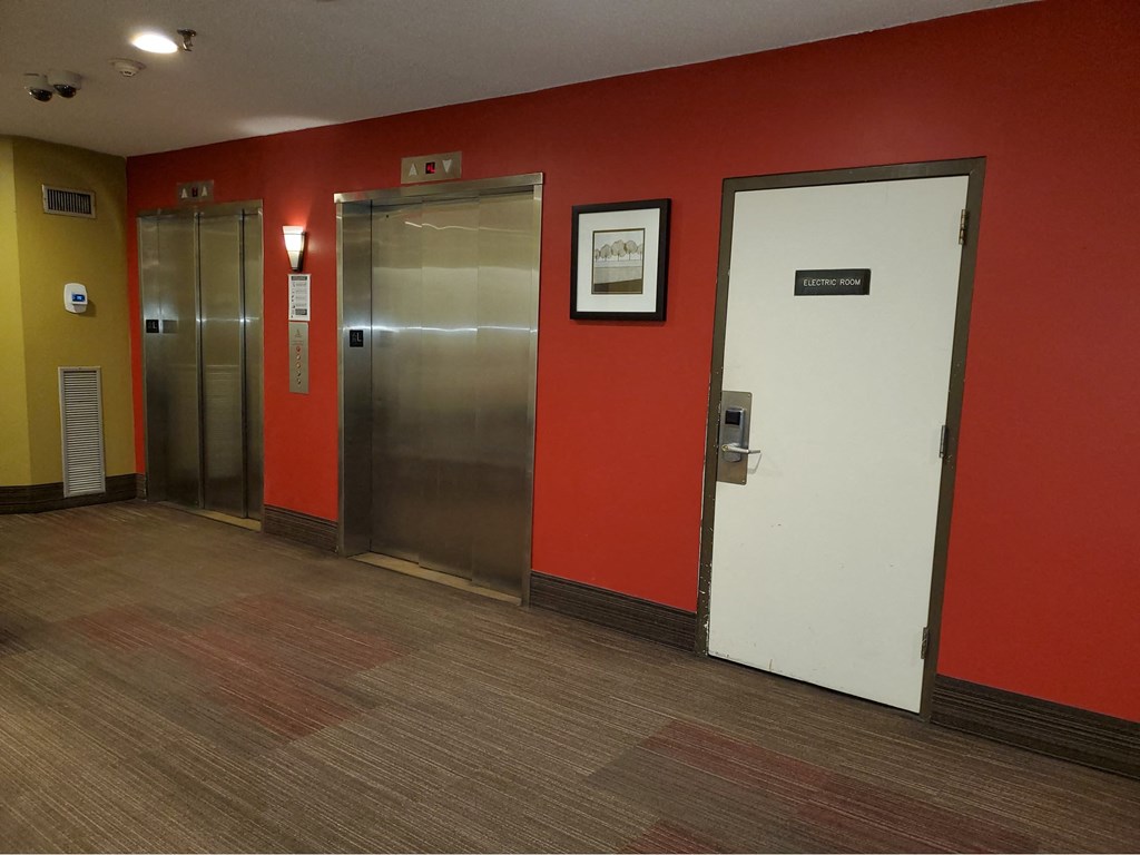 a hallway with red walls and stainless steel elevators and a door