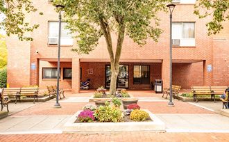 a courtyard with benches and a tree in front of a brick building