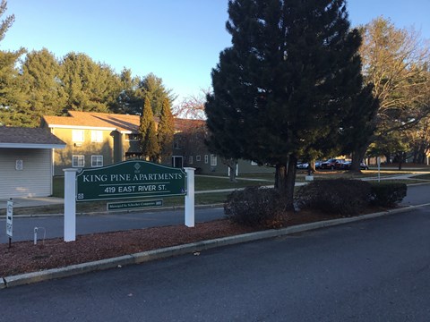 a sign for king pine apartments in front of a road and trees