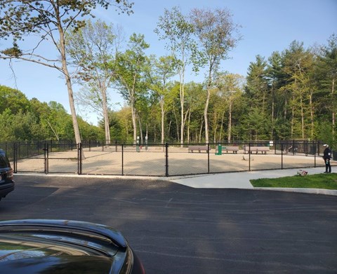 A black car is parked in a parking lot with a playground in the background.