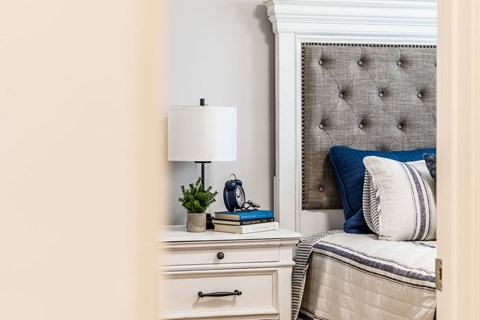 A bedroom with a bed, a nightstand with a lamp, and a plant.