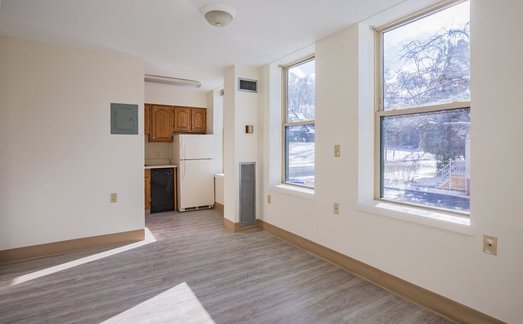 an empty living room with large windows and a kitchen