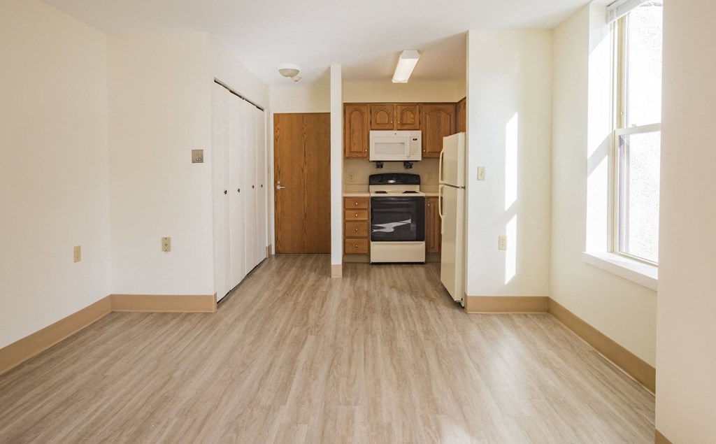 an empty living room and kitchen with wood floors and white walls