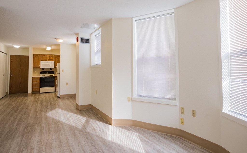 the living room and kitchen of an apartment with wood flooring and a large window