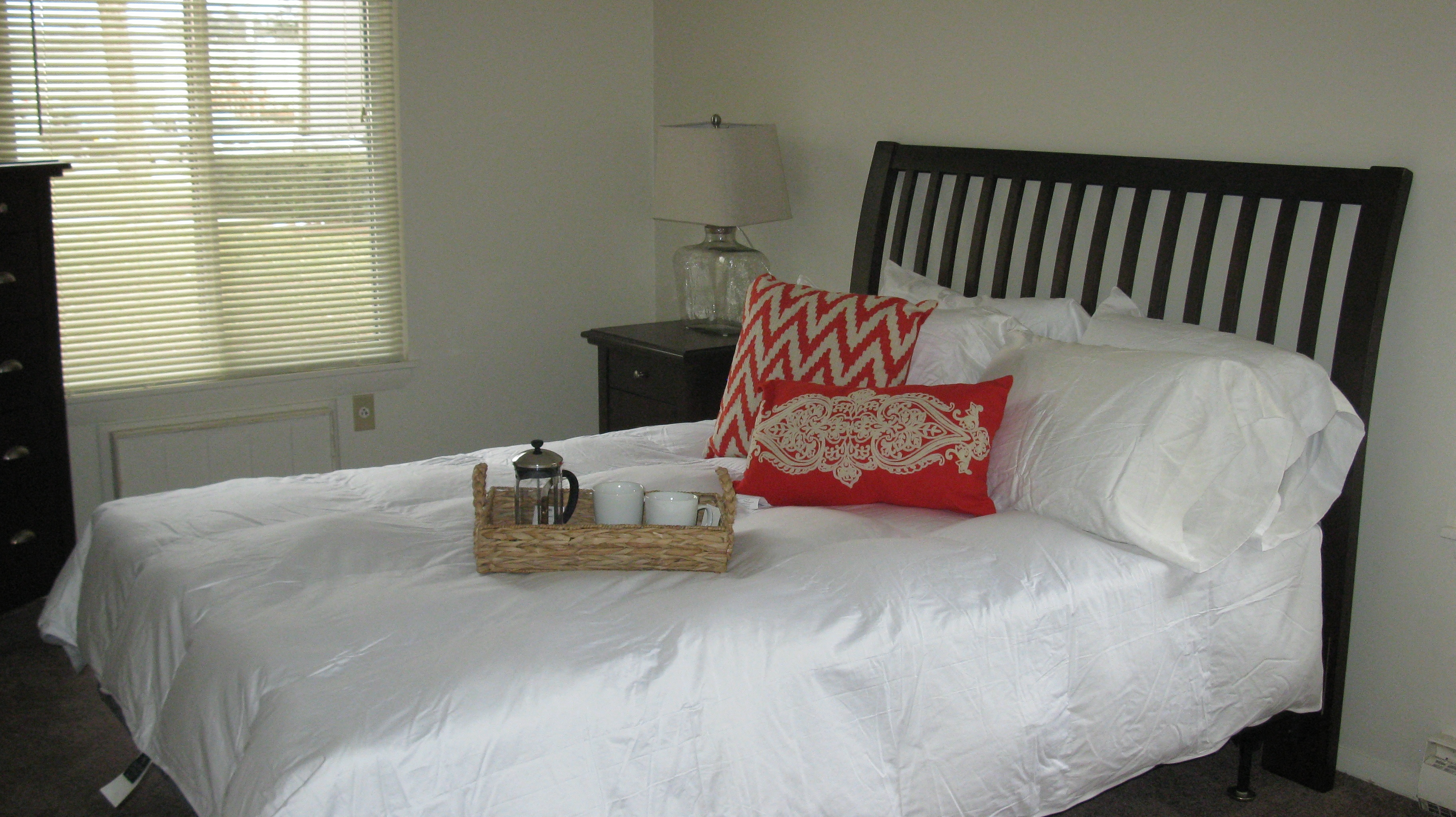 a bed with a white comforter and pillows and a basket of tea