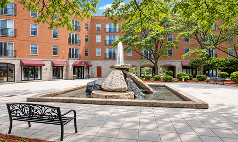 A fountain in the middle of a courtyard surrounded by benches and trees.