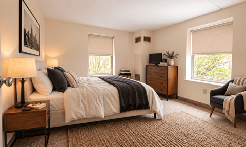 A bedroom with a large bed, a chair, and a window.
