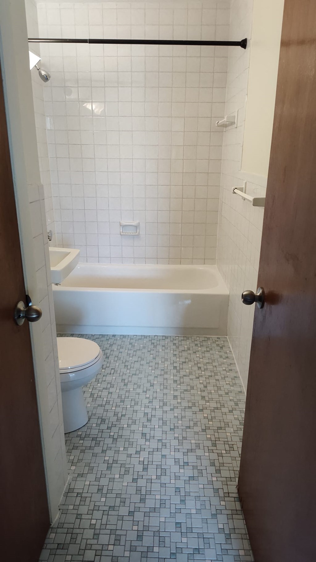 A white toilet is in a bathroom with a white tub and a tile floor.