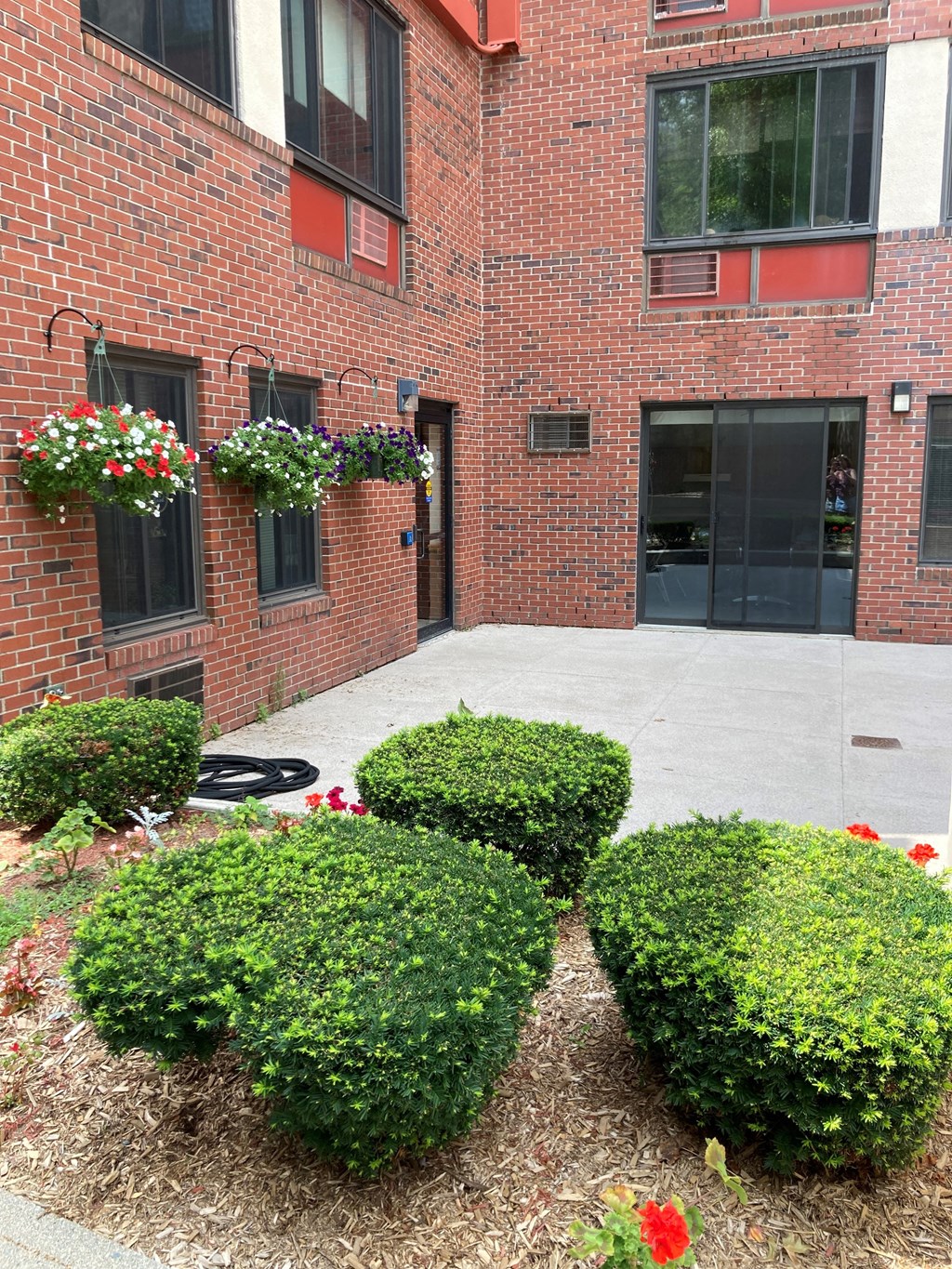 the front of a brick building with a sidewalk and plants