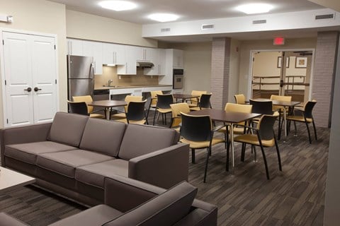 A room with a couch, chairs, and a kitchen area.