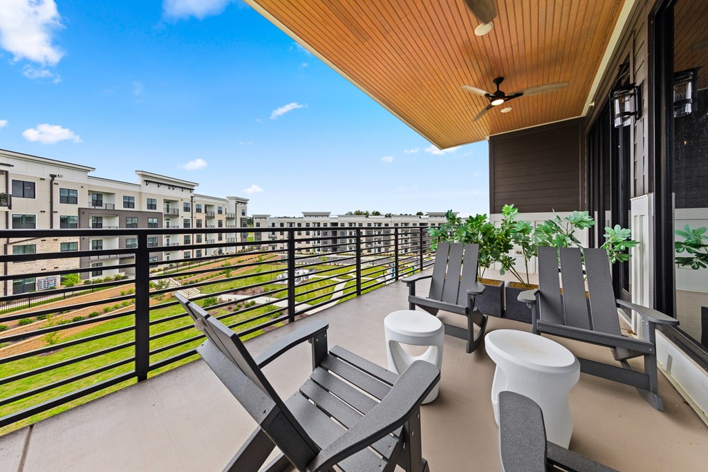 A balcony with chairs and a table is overlooking a row of buildings at Views at Flowers Apartments, Clayton, North Carolina