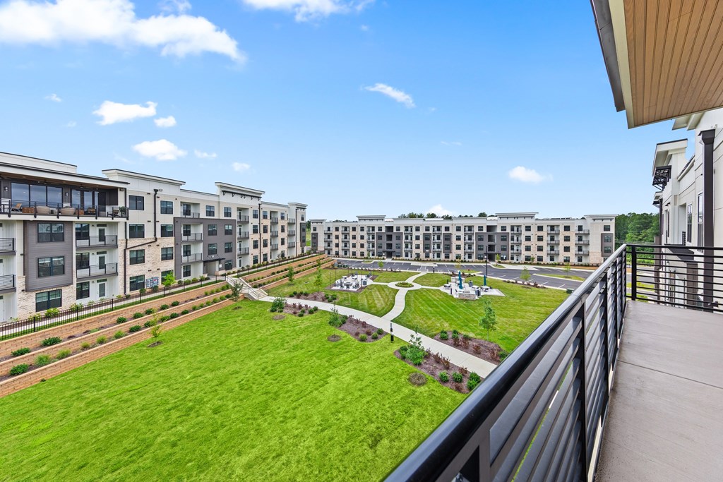 A view of a green lawn from a balcony with apartment buildings in the background at Views at Flowers Apartments, Clayton, North Carolina