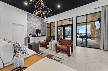 A modern living room with a grey sofa, a wooden coffee table, and a large window with a view of the city at Views at Flowers Apartments, Clayton, NC, 27527