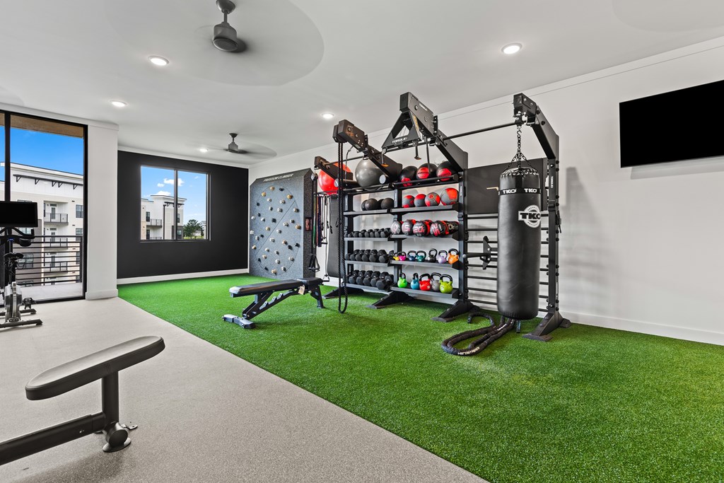 A home gym with a green artificial turf floor and a variety of exercise equipment at Views at Flowers Apartments, Clayton
