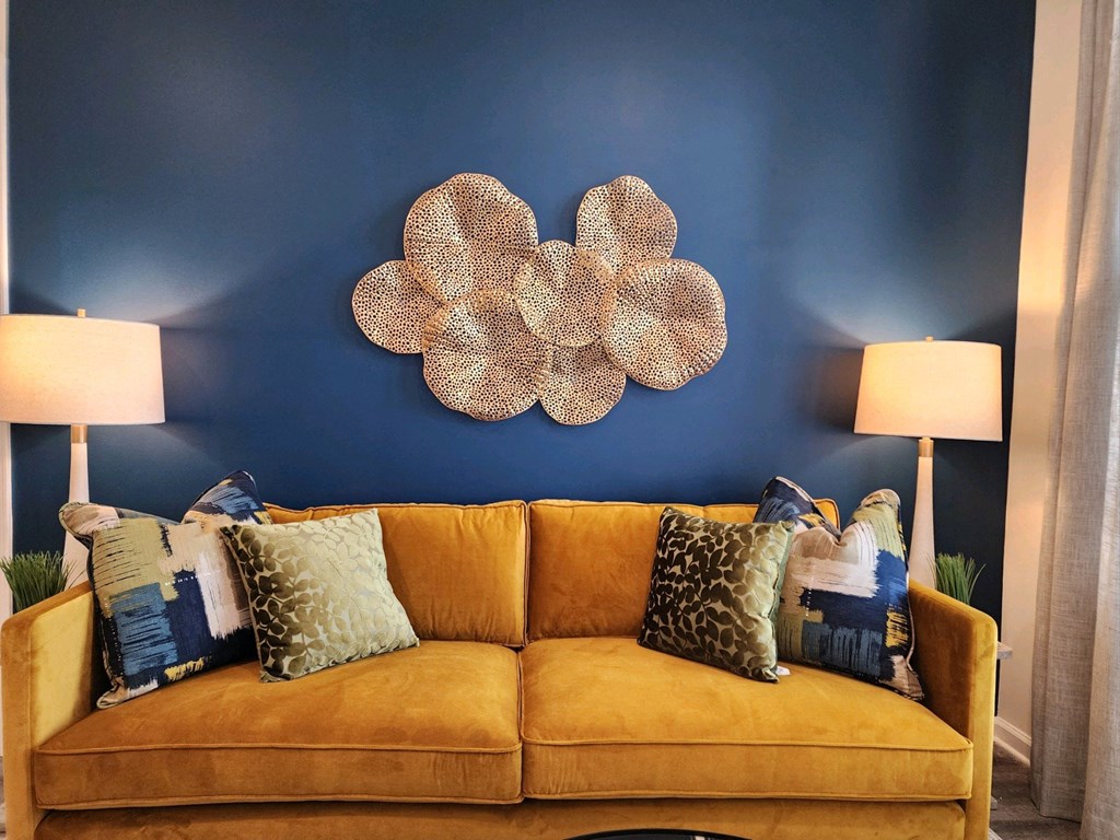 Couch with pillows in front of a blue wall with a flower on it at Ardmore at Topside in Louisville, TN 37777