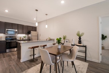 a dining area with a table and chairs and a kitchen in the background - Photo Gallery 3