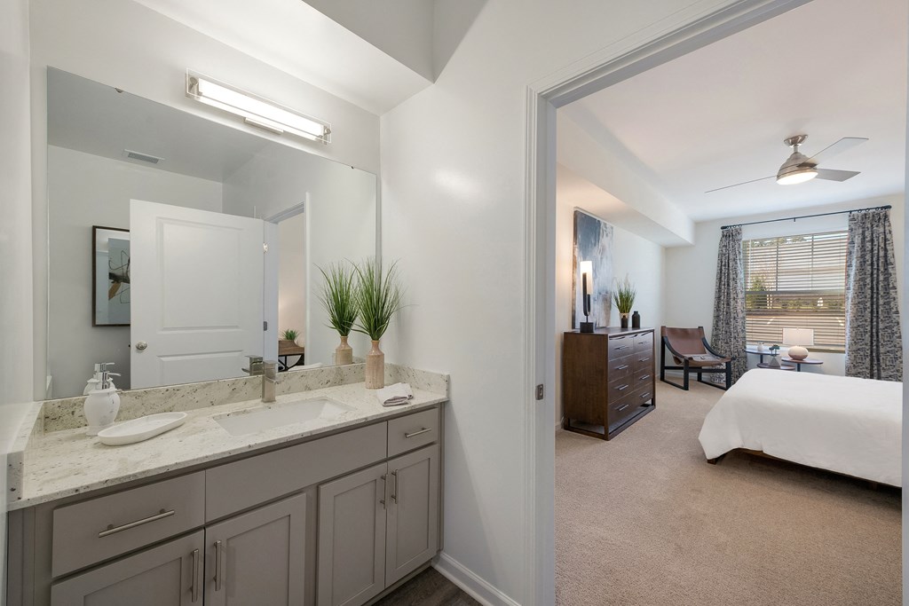 a bathroom with a sink and a mirror and a bedroom with a bed